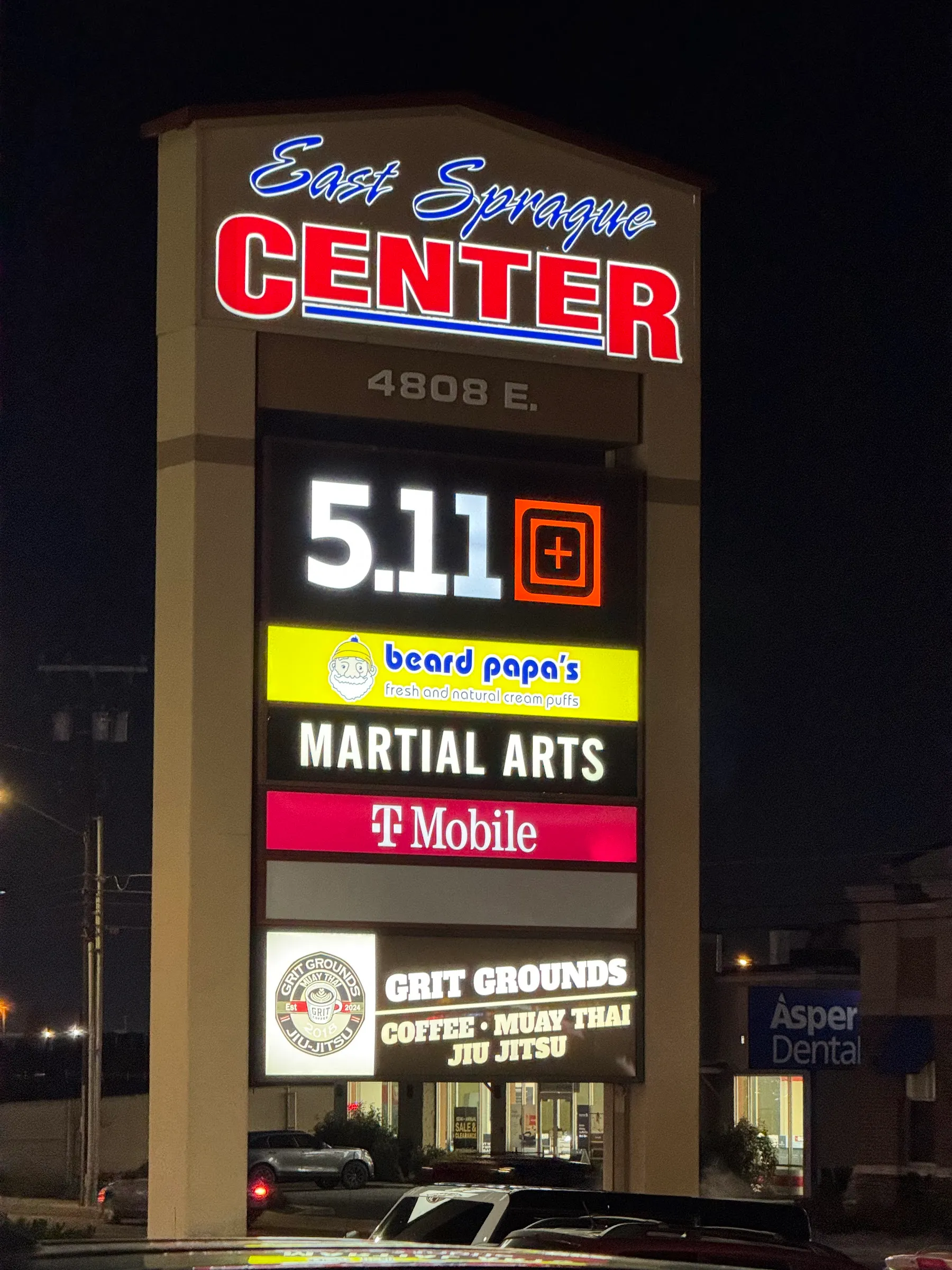 The East Sprague Center pylon sign at night with the Grit Grounds panel lit